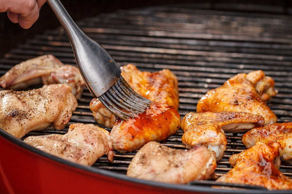 Brushing chicken wings with sauce on a Weber Grill – Tailgate food ideas