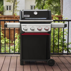 On a wooden deck, the Weber Spirit E-425 Gas Grill has a closed black lid with a built-in thermometer, two side tables, and four burner controls, including two red Boost Burner knobs for the Sear Zone.