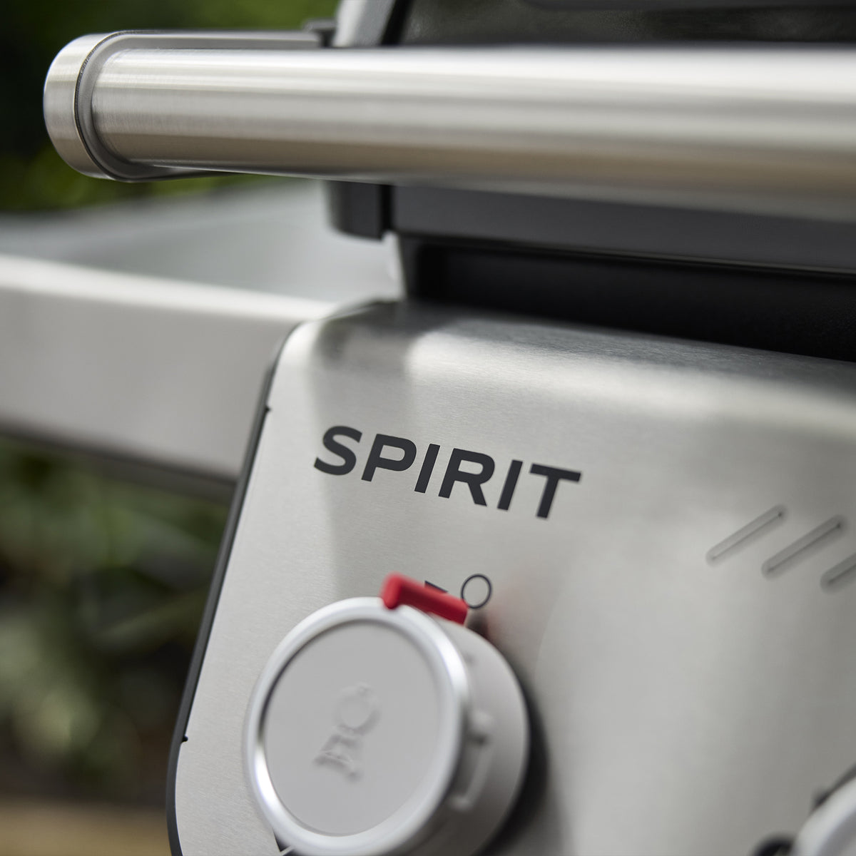 Close-up of the Weber Spirit E-310 Gas Grill’s silver control panel, showing the Spirit name, a burner control knob, and the lid handle.