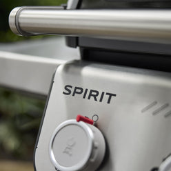Close-up of the Weber Spirit E-325 Gas Grill’s silver control panel, showing the Spirit name, a burner control knob, and the lid handle.
