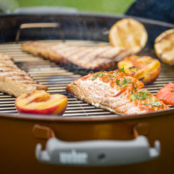 Weber 22” Original Kettle Premium charcoal grill cooks salmon, peaches, and lemon halves together for a grilled meal.