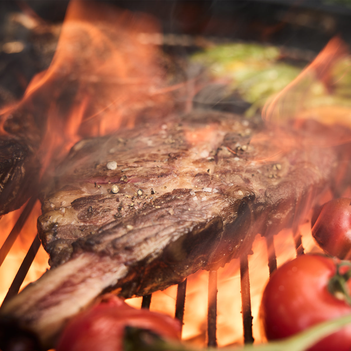 Direct charcoal heat sears a bone-in steak alongside vegetables on the green Weber 22” Original Kettle Premium charcoal grill.