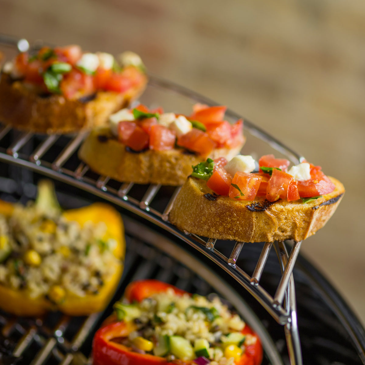 Toasted bread topped with tomatoes, cheese, and basil on the warming rack above stuffed bell peppers on the cooking grate.