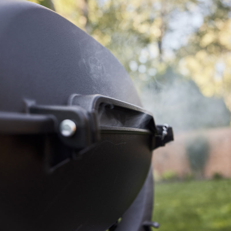 Close-up of smoke escaping through the rear vent beneath a gas grill’s closed domed lid.