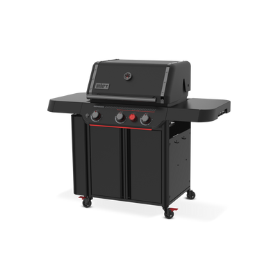 Front-right view of the matte black Weber Genesis E-330 Gas Grill Stealth Edition with the lid closed, two side tables, tool hooks, enclosed storage, and a red Sear Burner knob.