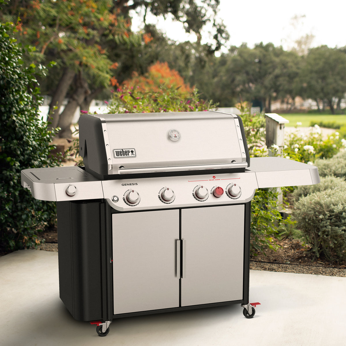 On a garden patio, the Weber Genesis S-435 Gas Grill has a closed stainless-steel lid, a covered side burner, a large prep table, and storage in a double-door cabinet and side grill locker.