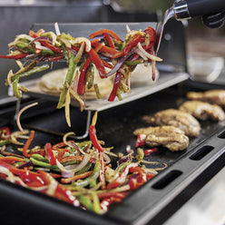 Weber Rust-Resistant Griddle Insert cooks chicken, peppers, and onions for fajitas, with a metal spatula lifting vegetables for serving.