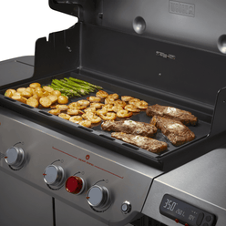 Steaks, shrimp, potatoes, and asparagus cooking together on the Weber Rust-Resistant Griddle Insert inside an open Genesis grill.