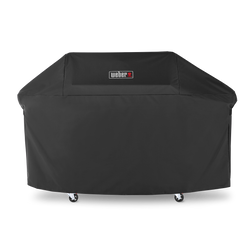 A centered Weber logo marks the black Premium Grill Cover, fitted over a Genesis grill’s lid, side tables, and cabinet with the casters exposed below.