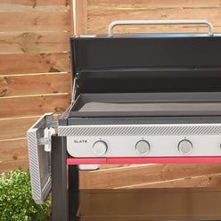 The folding side table on the Weber Slate 36” Rust-Resistant Griddle is lowered for compact storage, with the hard cover open above the pre-seasoned cooktop.