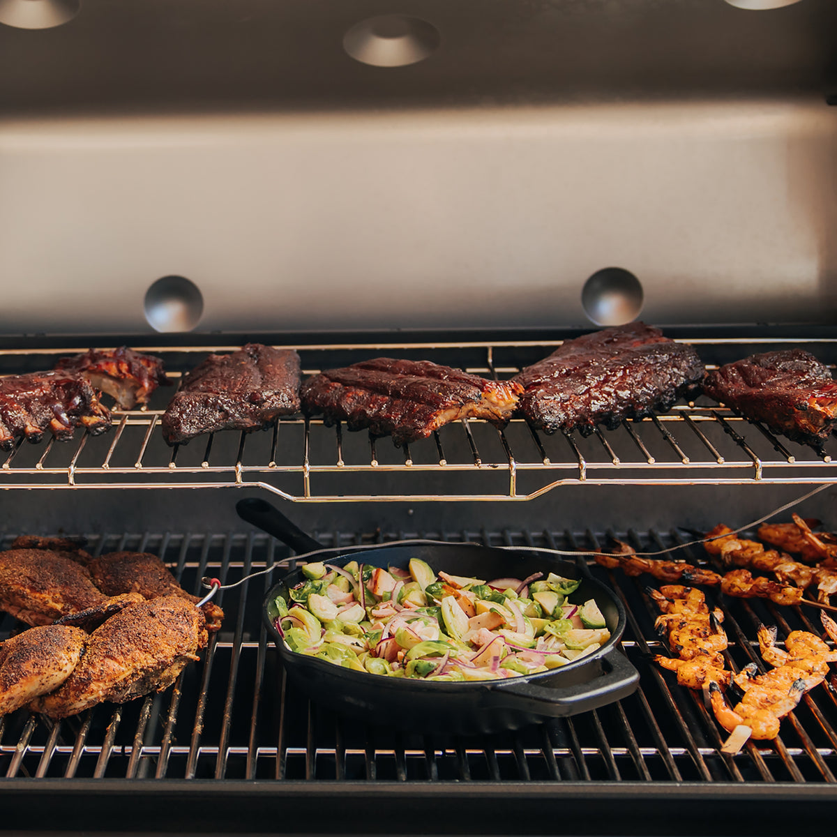 Ribs rest on the expandable top cooking grate of the Weber Genesis S-435 Gas Grill while chicken, shrimp skewers, and a skillet of vegetables cook below.