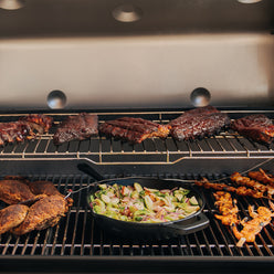 Ribs rest on the expandable top cooking grate of the Weber Genesis S-435 Gas Grill while chicken, shrimp skewers, and a skillet of vegetables cook below.